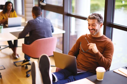 Man on laptop with his feet on a table smiling
